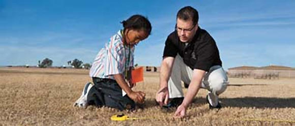 A man teaches a young boy on water conservation techniques in a large dry field.