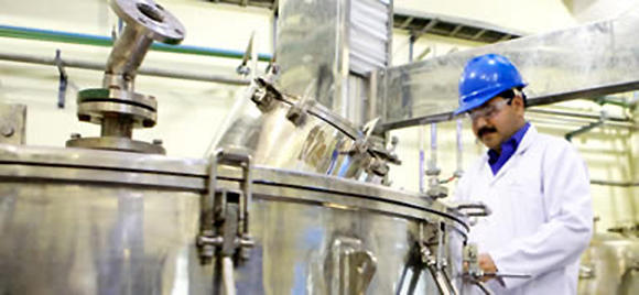 An Indian man with a mustache and laboratory safety clothing examines a large piece of machinery.