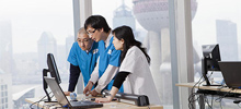 Three hospital workers congregate around a computer in an office with the view of Shanghai.